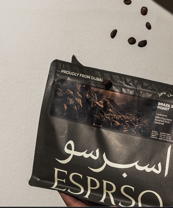 A hand holding a bag of ESPRSO Brazil Espresso Roast, beans falling from above