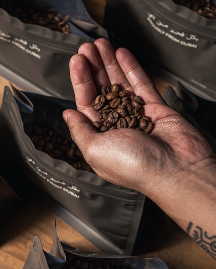 A hand holding roasted coffee beans above open ESPRSO bags